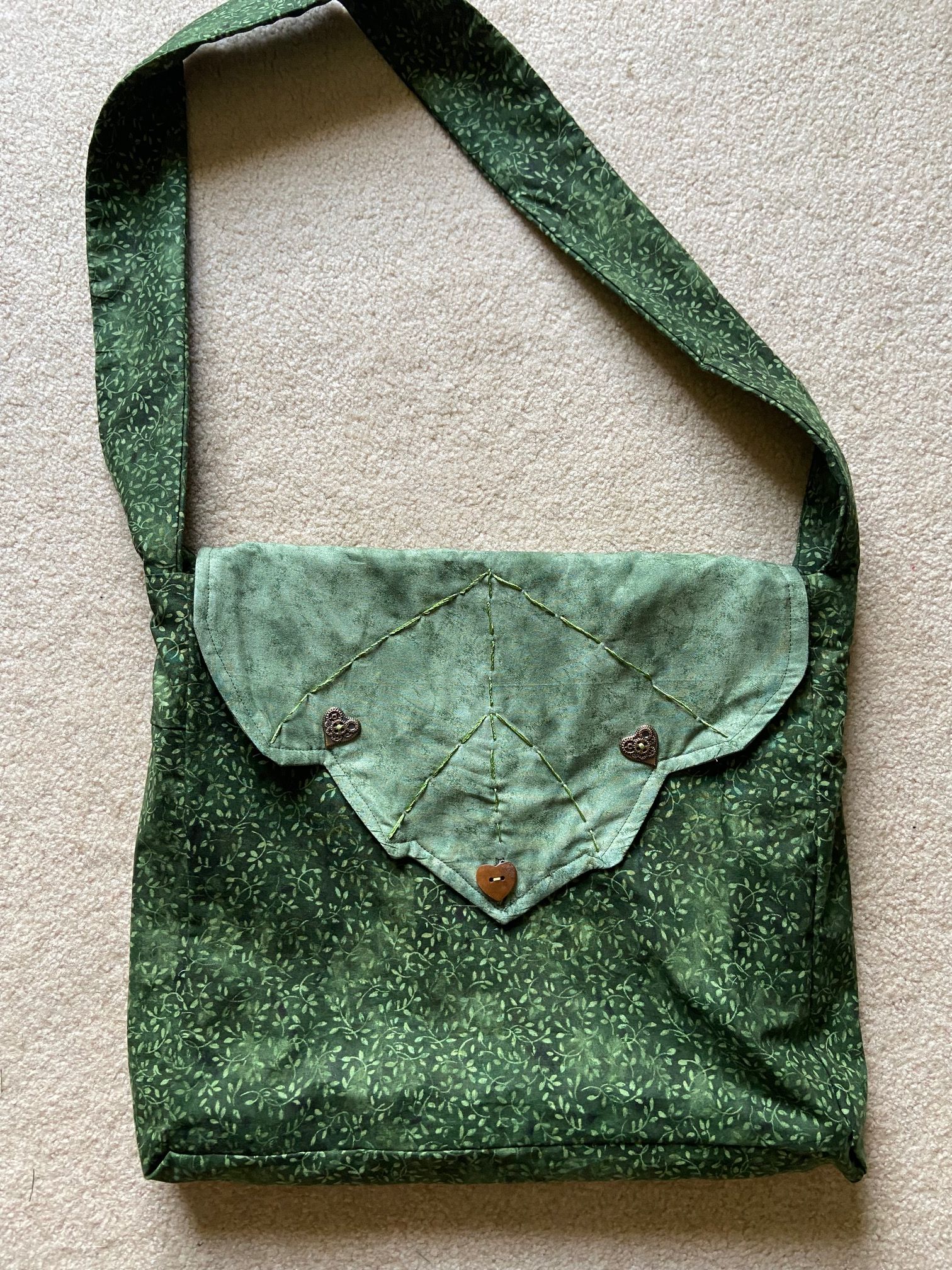 A hand sewn green tote bag shaped like a leaf with heart shaped buttons