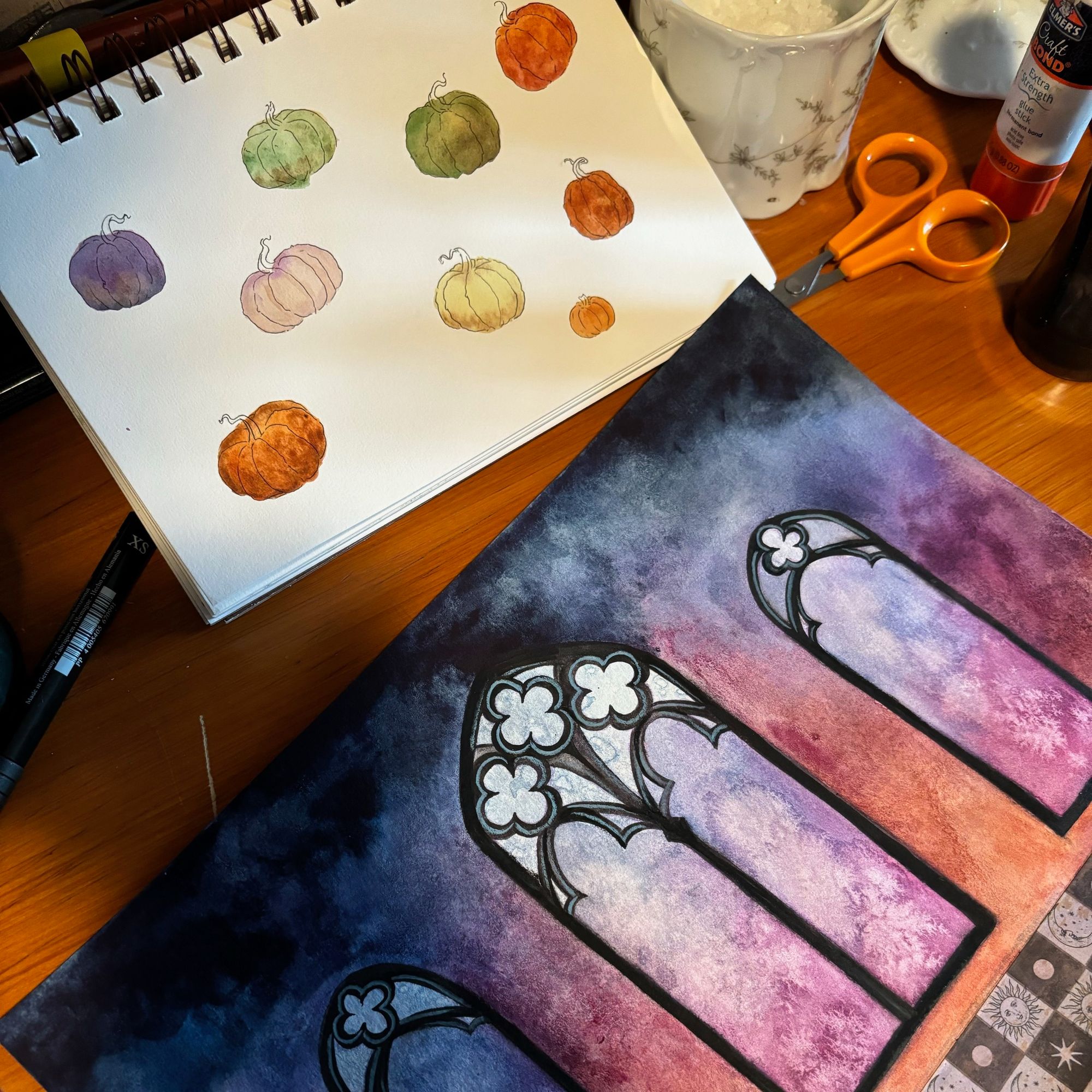 Two watercolor paintings, one of 9 pumpkins, the other 3 gothic windows above a checkered floor